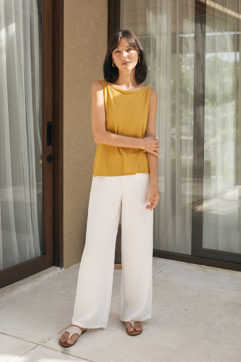 Woman wearing a mustard yellow cotton sleeveless top and white pants standing  in resort in bali