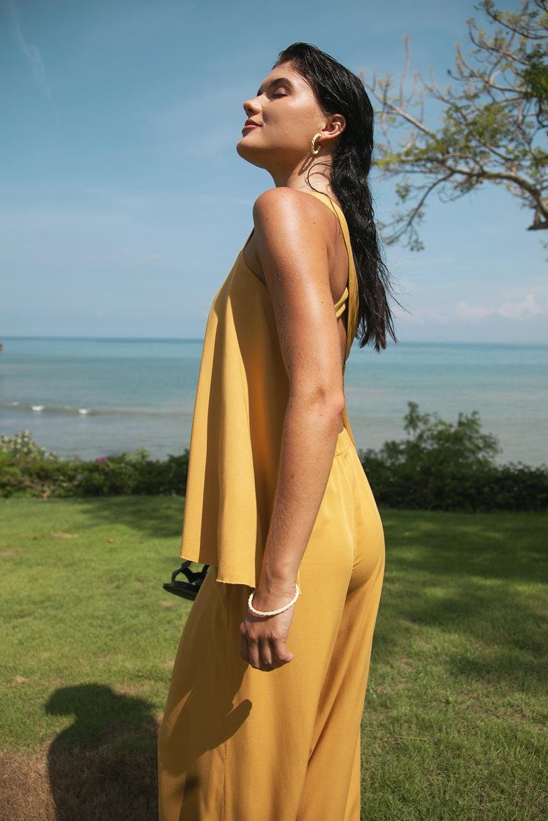 A woman wearing a flowing mustard yellow sleeveless set up stands outdoors on a grassy area in bali five star resort hotel