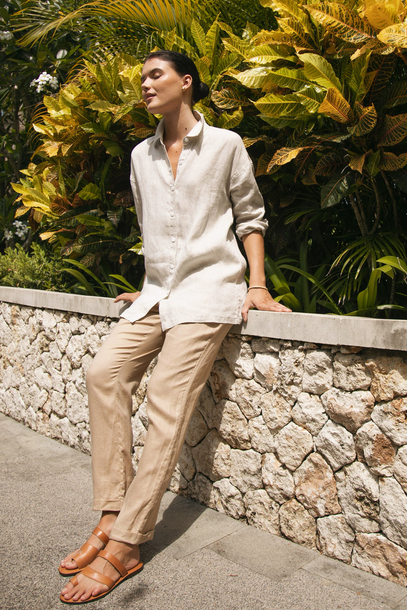 women wearing by the sea linen beige pants and linen shirt sitting in front of plants n the luxury 5start hotel 