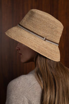 Woman wearing the natural straw Dewy hat with a brown ribbon in a tropical resort setting
