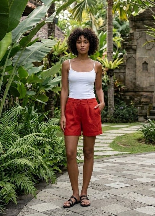 Woman in a white tank top and red linen shorts standing in a lush resort in Bali