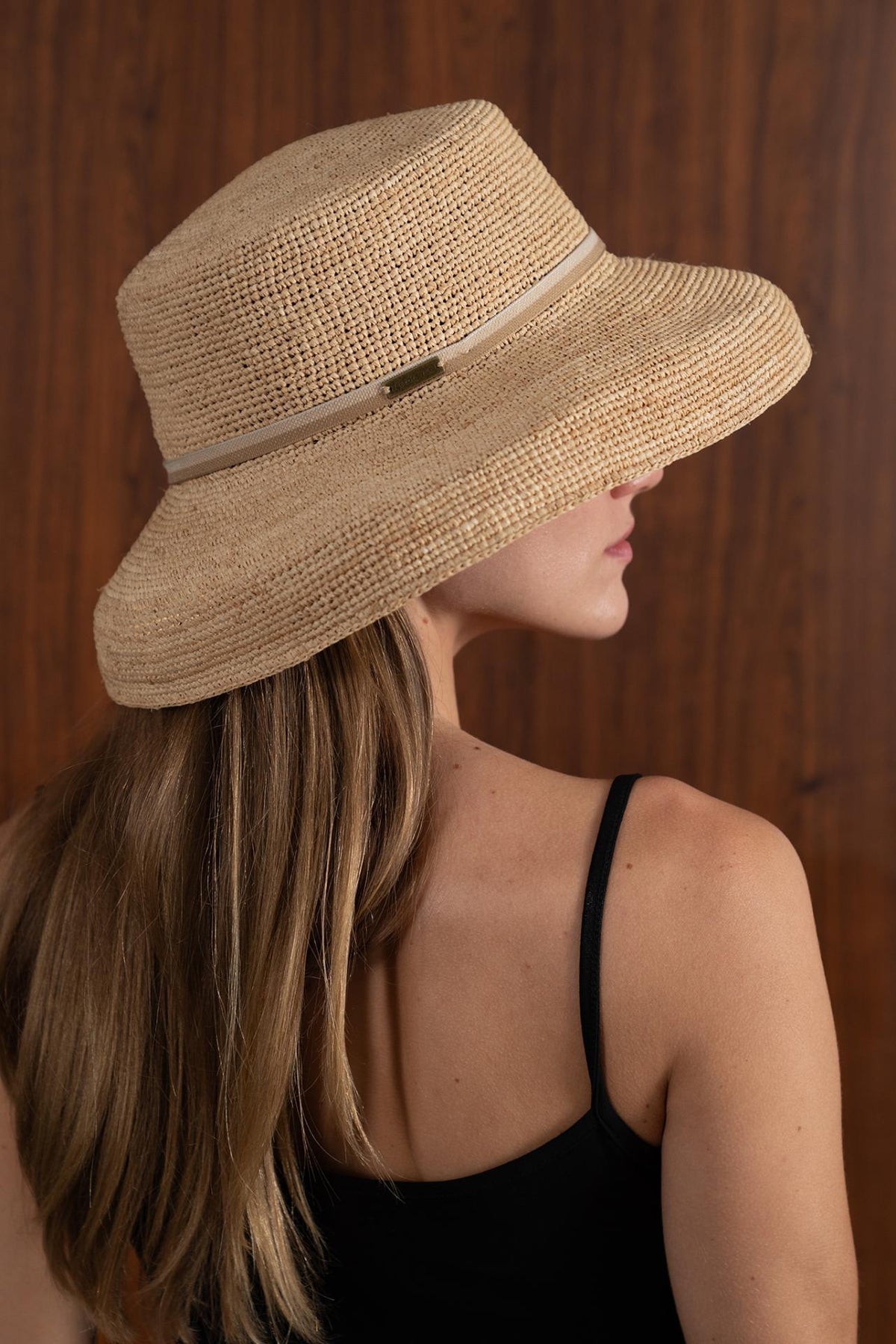 Woman wearing the natural straw Keira hat with a creme ribbon in a tropical resort setting