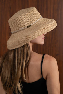 Woman wearing the natural straw Keira hat with a creme ribbon in a tropical resort setting
