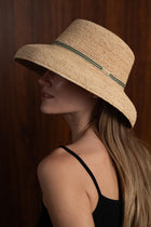 Woman wearing the natural straw Keira hat with a green ribbon in a tropical resort setting