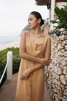 Model wearing the pale yellow linen Linda midi dress in a tropical resort setting