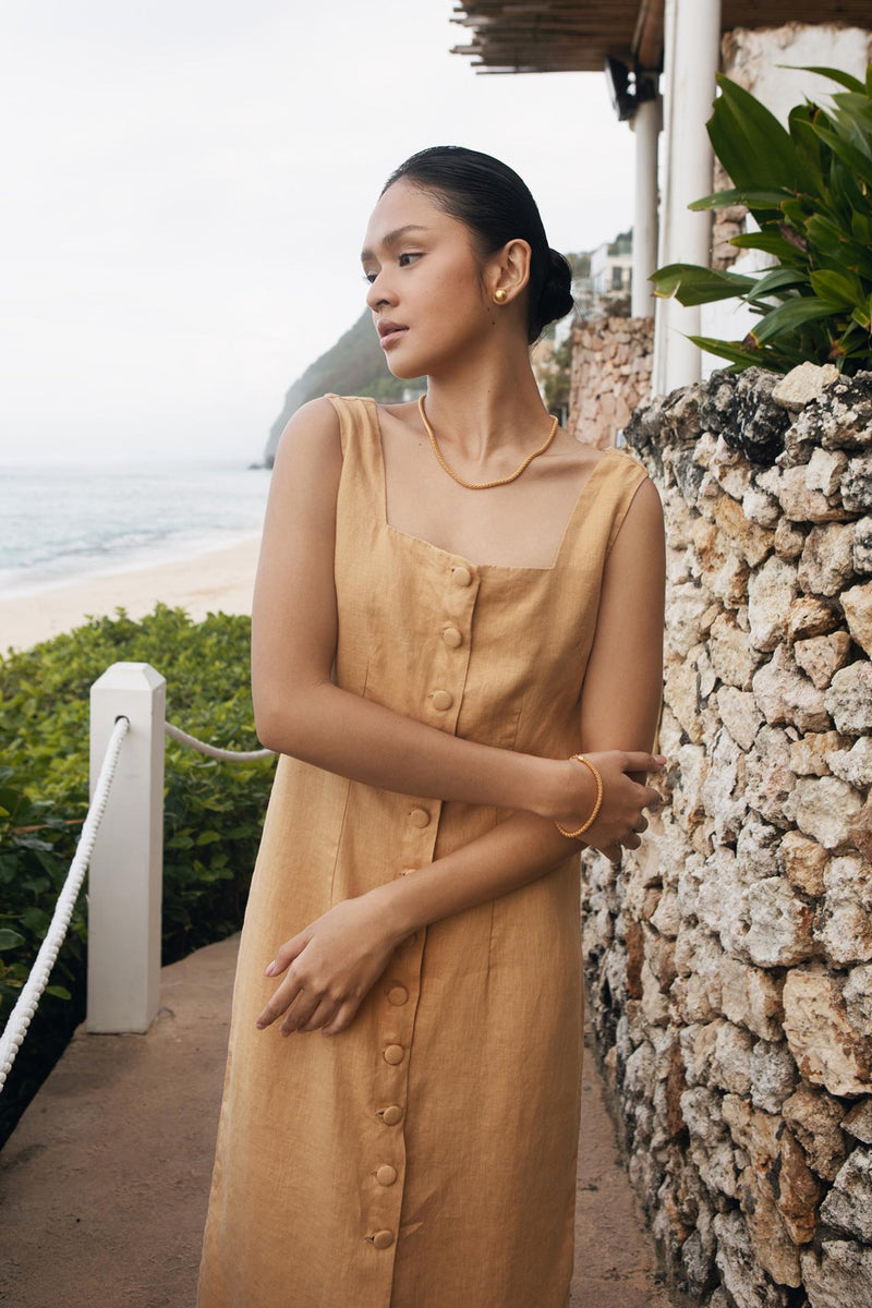 Model wearing the pale yellow linen Linda midi dress in a tropical resort setting