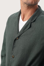 Close-up of the linen fabric texture and refined tailoring details on the dark green jacket
