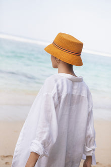 Luxury resort styling featuring the Moa Raffia Bucket Hat Tangerine in a tropical coastal setting