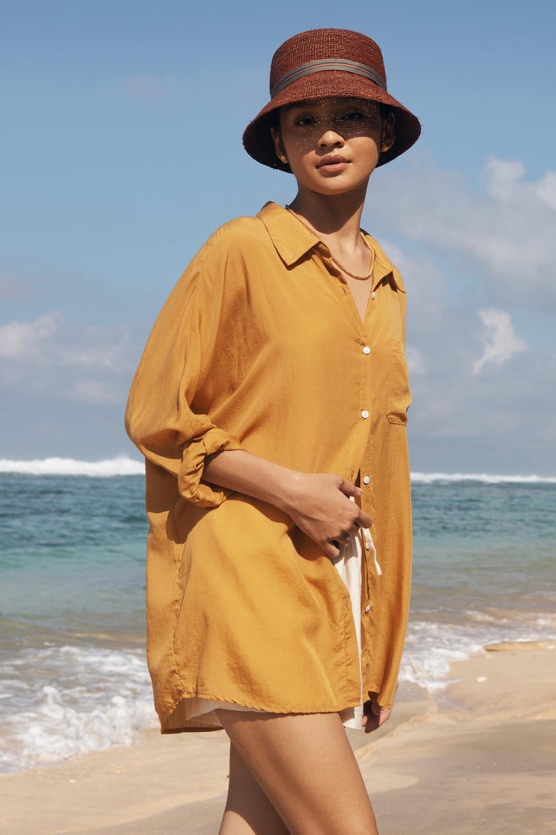 Model wearing the mustard muara shirt in a tropical resort setting
