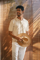 Model wearing the By The Sea Bali Rado cream cotton-knit polo shirt in a relaxed coastal lifestyle setting