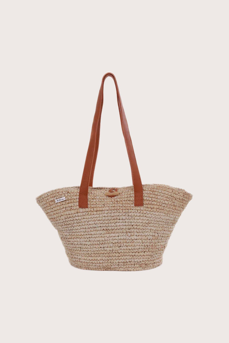 Straw bag jerami in natural handwoven finish styled as a refined resort accessory, front view