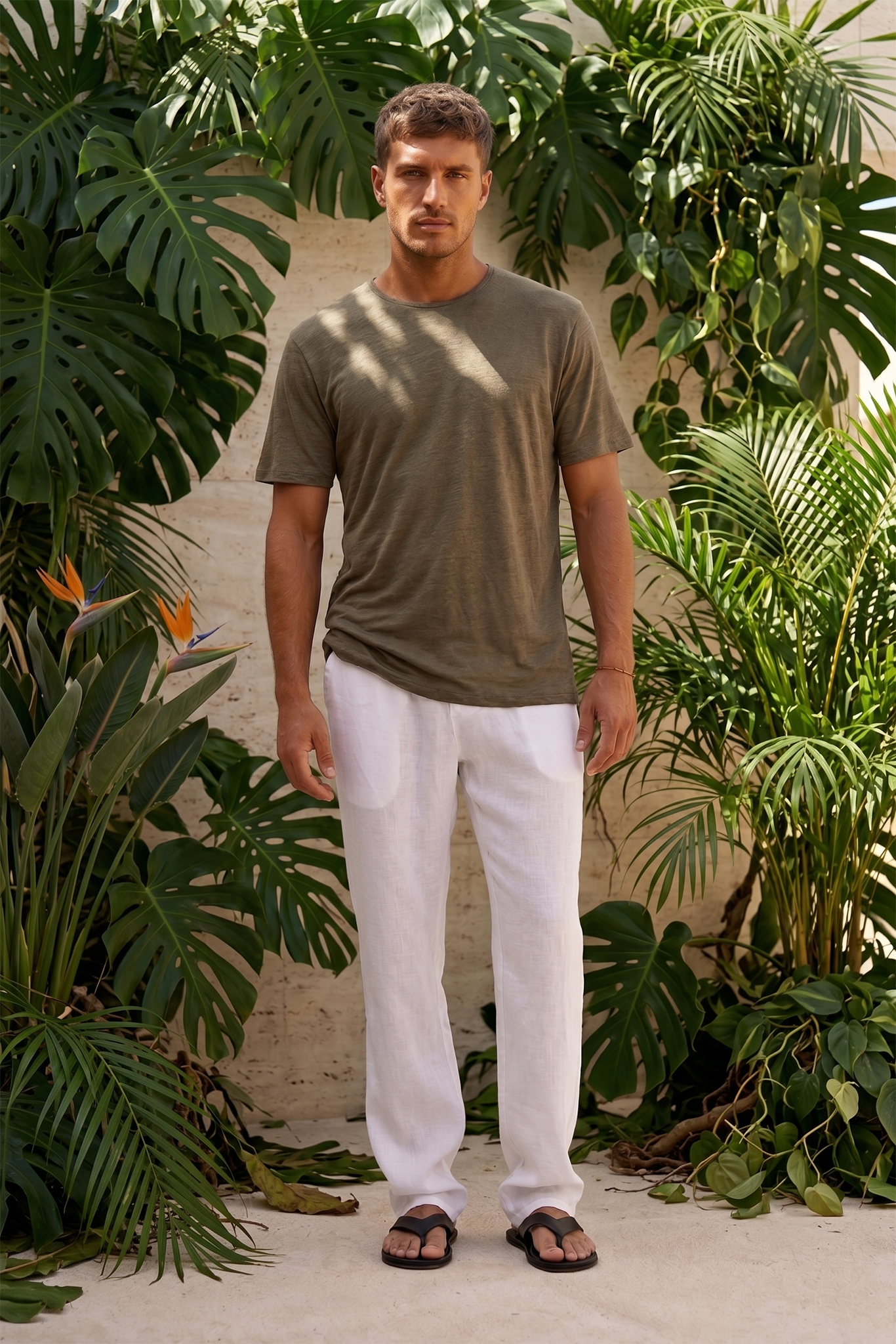 By the sea bali Man wearing a linen jersey green t-shirt and white linen pants standing among Bali resort tropical plants.