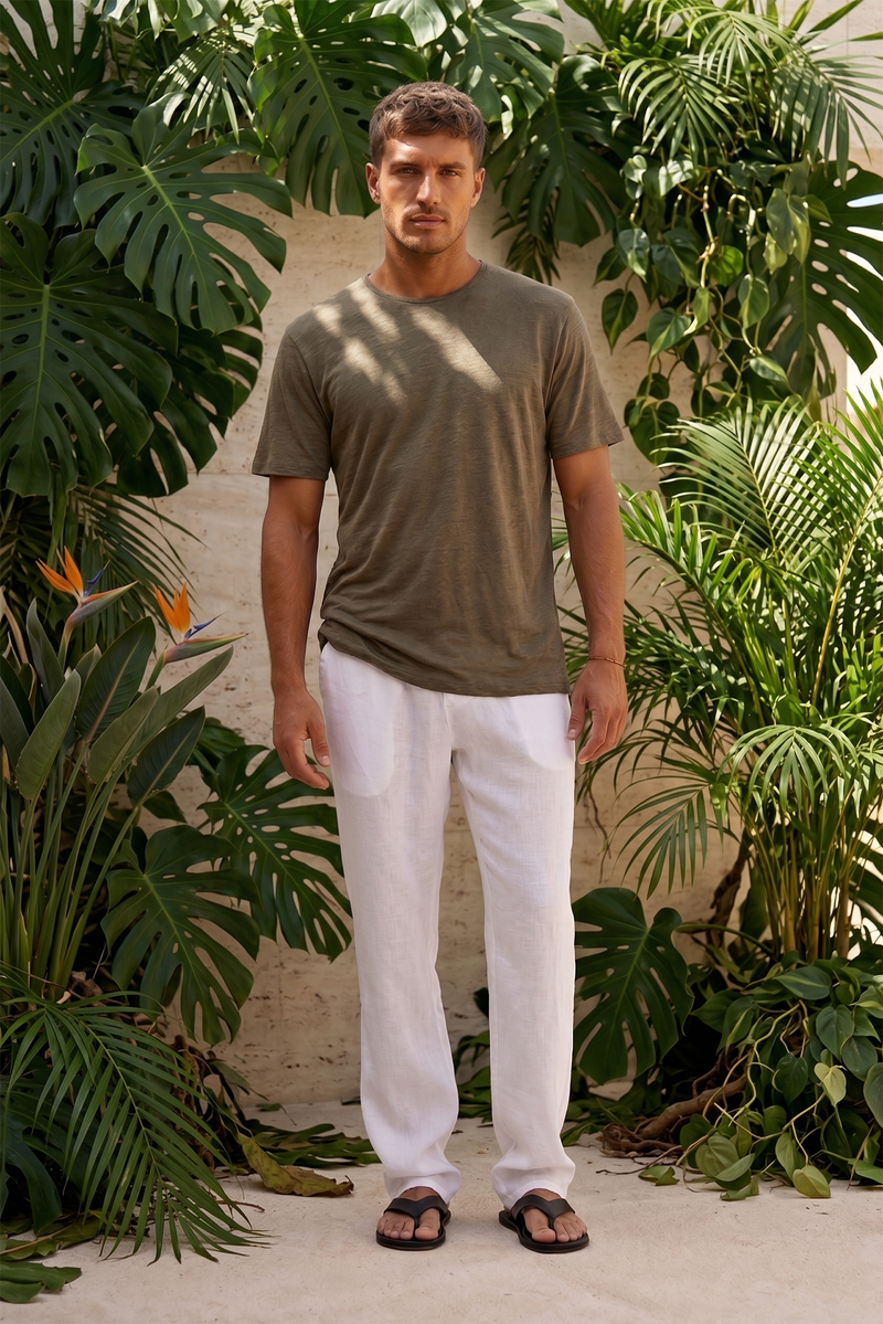 By the sea bali Man wearing a linen jersey green t-shirt and white linen pants standing among Bali resort tropical plants.